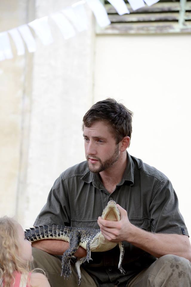 Tom Covell holding a freshwater crocodile while talking with a child